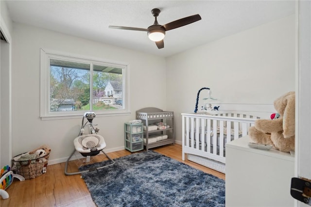 bedroom featuring baseboards, a ceiling fan, a crib, and wood finished floors
