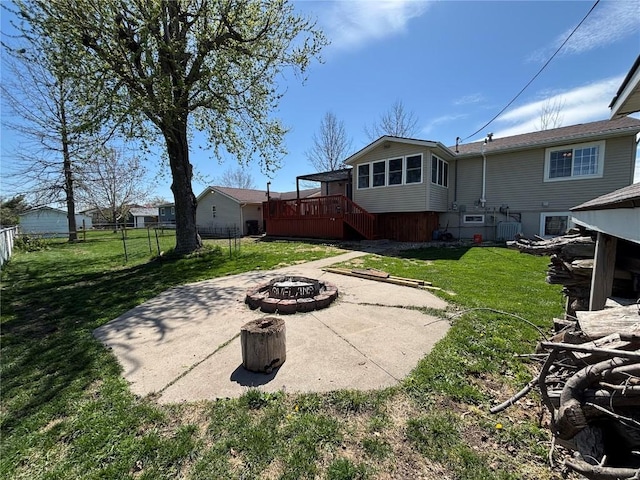 rear view of house with a wooden deck, a patio area, fence, a yard, and a fire pit