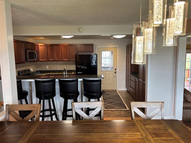 kitchen featuring a healthy amount of sunlight, a kitchen bar, dark countertops, a peninsula, and stainless steel appliances