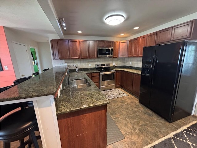 kitchen with a sink, a breakfast bar area, dark stone countertops, stainless steel appliances, and backsplash