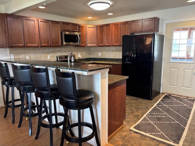 kitchen featuring decorative backsplash, a peninsula, black refrigerator with ice dispenser, a kitchen breakfast bar, and stainless steel microwave