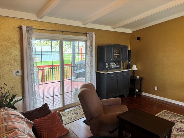 living room featuring wood finished floors, baseboards, beam ceiling, and visible vents