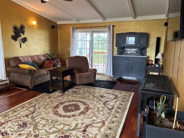 living room with ceiling fan, dark wood-style flooring, a wood stove, lofted ceiling with beams, and a textured wall