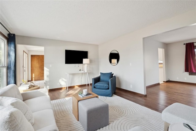 living room featuring a textured ceiling, baseboards, and wood finished floors