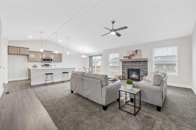 living room featuring a glass covered fireplace, lofted ceiling, wood finished floors, baseboards, and a ceiling fan
