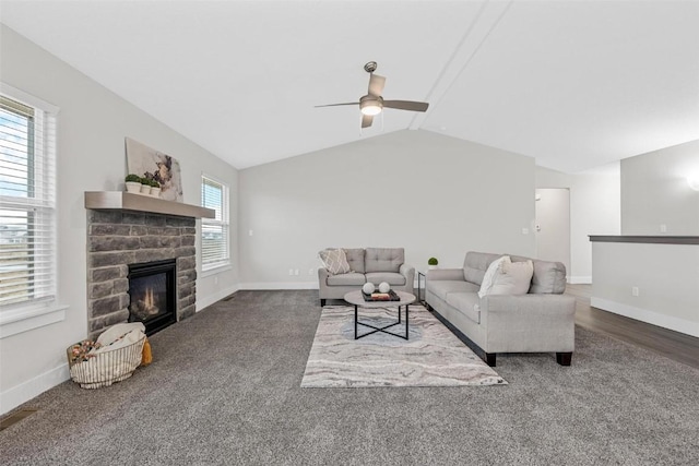 carpeted living area with a ceiling fan, baseboards, vaulted ceiling, and a stone fireplace