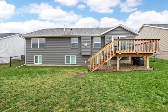 rear view of house with fence, roof with shingles, stairs, a deck, and a lawn