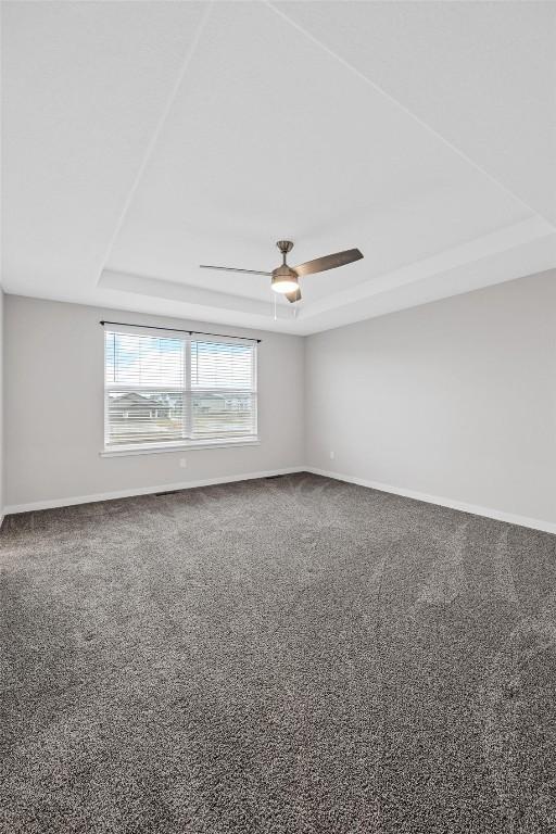 empty room featuring carpet flooring, a tray ceiling, ceiling fan, and baseboards