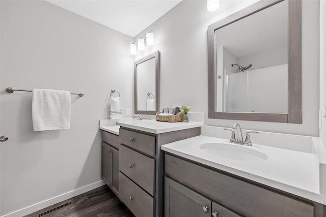 bathroom featuring visible vents, walk in shower, wood finished floors, two vanities, and a sink