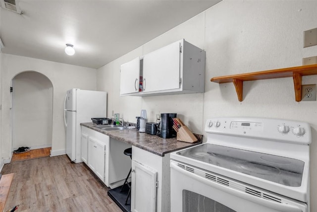 kitchen featuring visible vents, a sink, light wood finished floors, white appliances, and white cabinetry