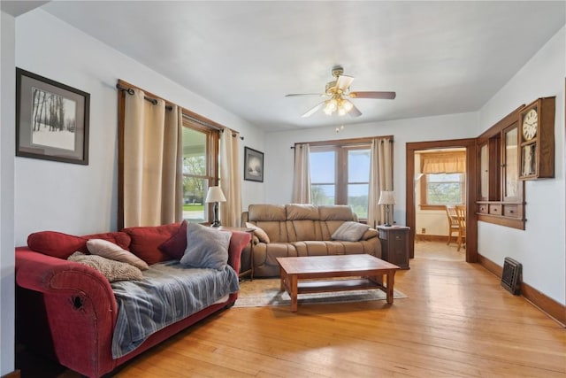 living area featuring plenty of natural light, a ceiling fan, baseboards, and light wood-style flooring