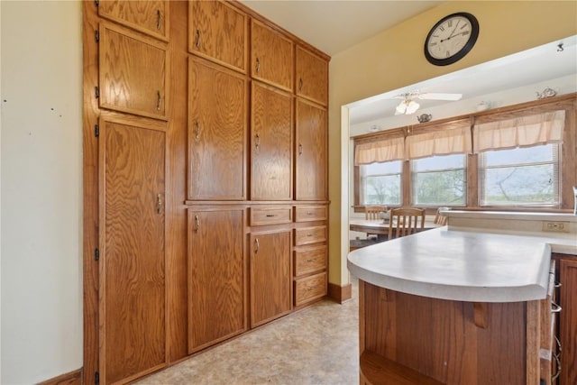 kitchen with light countertops, ceiling fan, brown cabinetry, and a peninsula