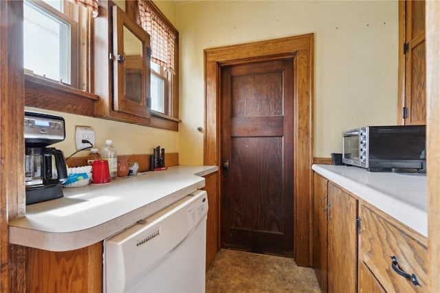 kitchen with white dishwasher, brown cabinets, a healthy amount of sunlight, and light countertops