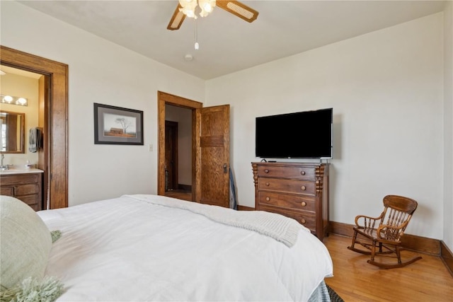 bedroom featuring a ceiling fan, baseboards, wood finished floors, and ensuite bath
