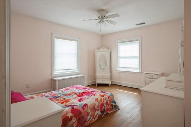 bedroom with baseboards, visible vents, radiator heating unit, and wood finished floors