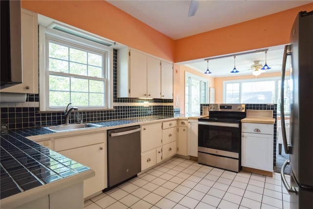 kitchen with ceiling fan, a sink, stainless steel appliances, tile countertops, and decorative backsplash