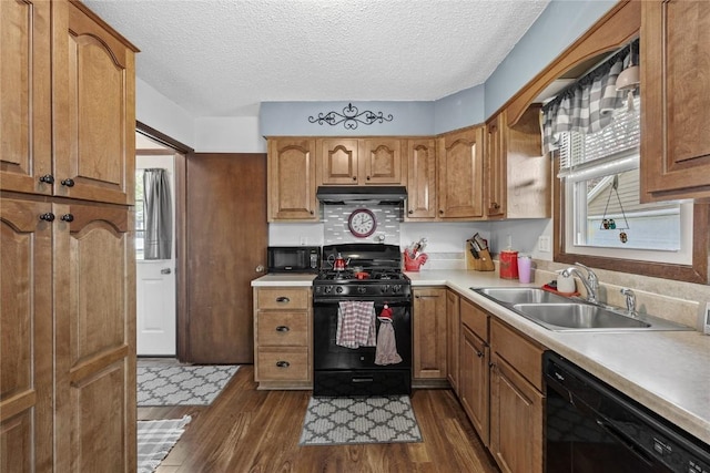 kitchen featuring a sink, light countertops, dark wood finished floors, under cabinet range hood, and black appliances
