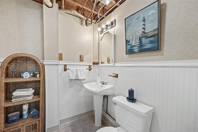 bathroom with tile patterned floors, a wainscoted wall, and toilet