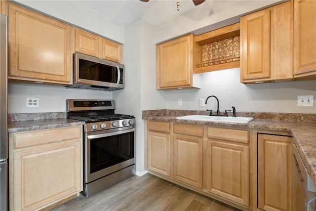 kitchen with light brown cabinetry, appliances with stainless steel finishes, light wood-style floors, and a sink