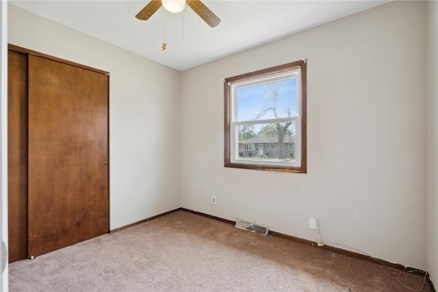 unfurnished bedroom featuring a ceiling fan, light colored carpet, visible vents, baseboards, and a closet