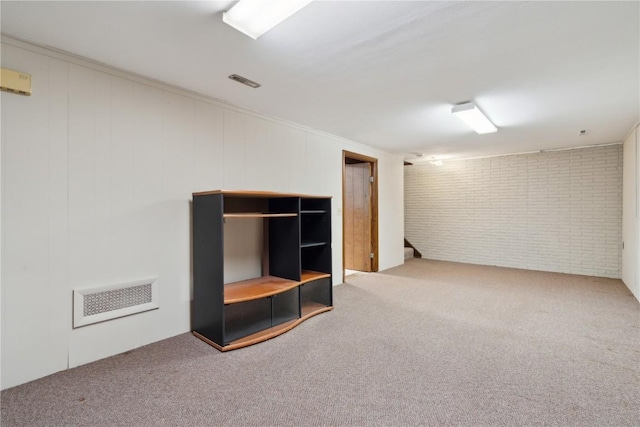 finished basement with carpet floors, brick wall, stairs, visible vents, and ornamental molding
