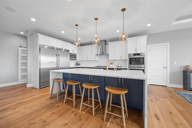 kitchen featuring white cabinets, wall chimney range hood, light wood-style floors, built in appliances, and baseboards