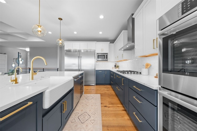 kitchen featuring blue cabinets, wall chimney exhaust hood, built in appliances, and white cabinets