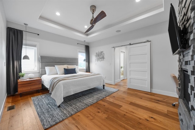 bedroom with a barn door, a raised ceiling, baseboards, visible vents, and hardwood / wood-style flooring