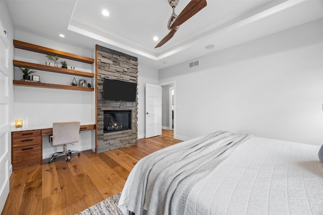 bedroom featuring built in desk, recessed lighting, wood finished floors, a tray ceiling, and visible vents