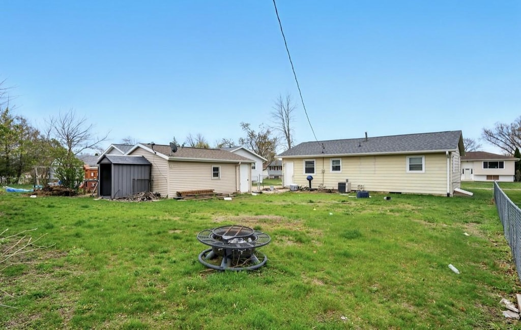 rear view of house featuring fence, a storage unit, an outdoor fire pit, an outbuilding, and a lawn