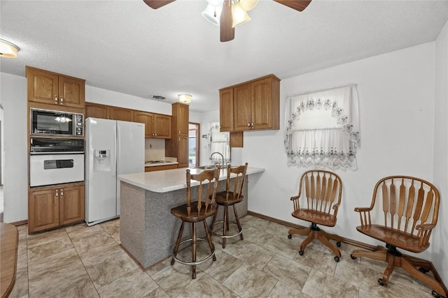 kitchen featuring white appliances, a ceiling fan, brown cabinetry, and a peninsula