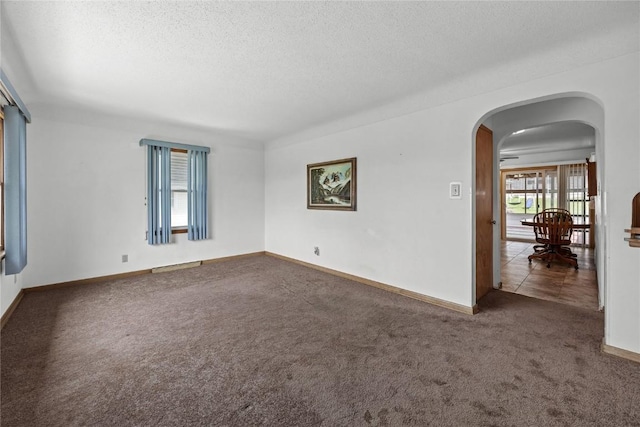 spare room with arched walkways, baseboards, a textured ceiling, and carpet floors