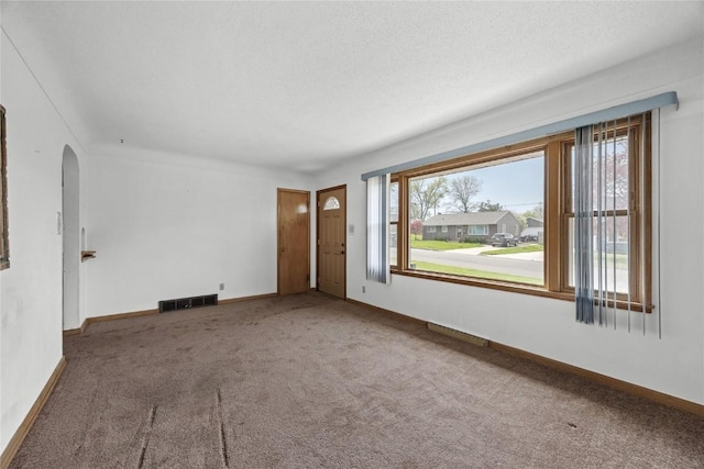 unfurnished living room with carpet floors, arched walkways, visible vents, and a healthy amount of sunlight