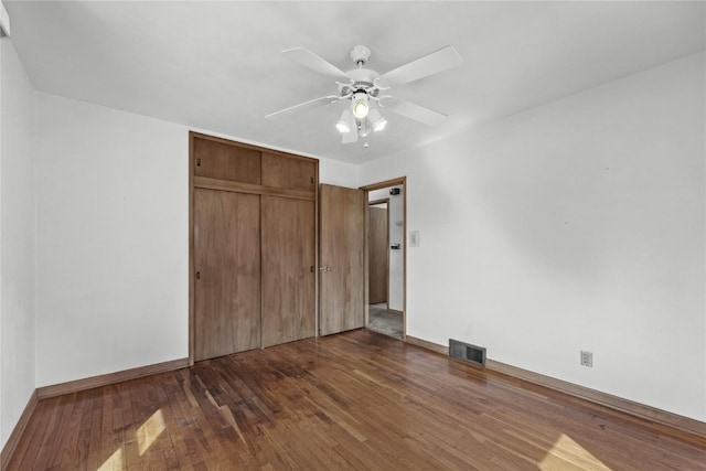 unfurnished bedroom with visible vents, a closet, wood finished floors, baseboards, and ceiling fan