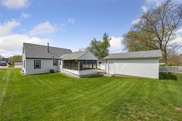 rear view of house with a lawn, a sunroom, central AC, fence, and an outdoor structure