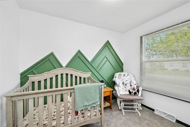 bedroom with a crib, carpet flooring, a textured ceiling, and visible vents