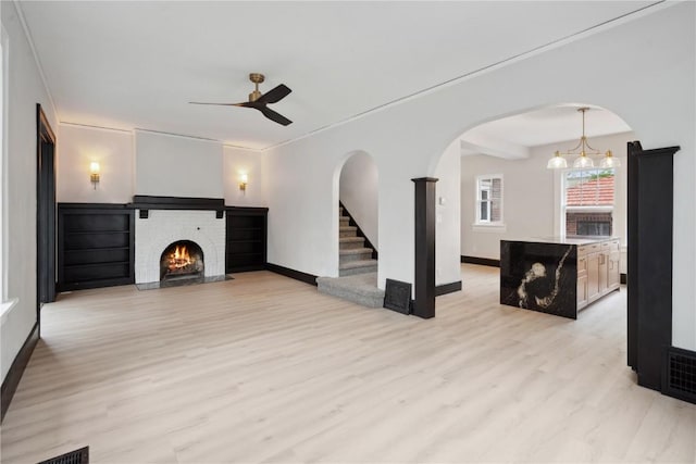 unfurnished living room with light wood-type flooring, baseboards, ceiling fan with notable chandelier, and a fireplace