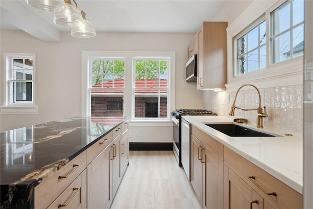 kitchen with light stone counters, tasteful backsplash, a sink, light wood-type flooring, and range with gas cooktop