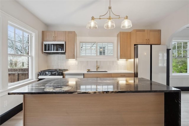 kitchen with a sink, light brown cabinets, arched walkways, freestanding refrigerator, and stainless steel microwave