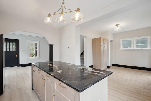 kitchen featuring arched walkways, baseboards, dark stone countertops, and light wood-type flooring