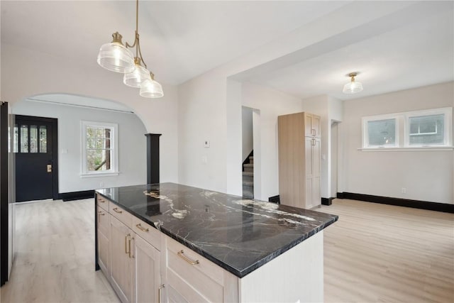 kitchen featuring arched walkways, hanging light fixtures, light wood-type flooring, baseboards, and dark stone countertops