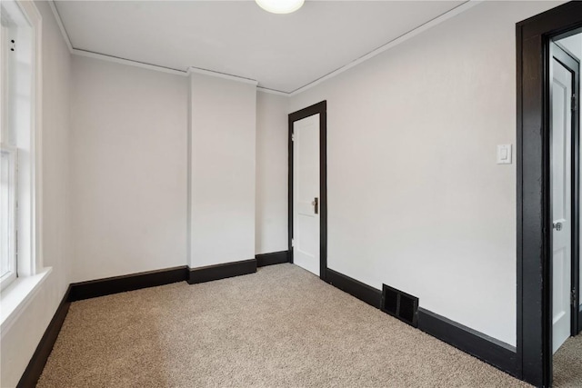 carpeted spare room featuring baseboards, ornamental molding, and visible vents