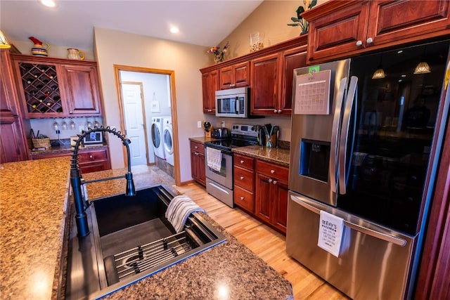 kitchen with dark brown cabinets, separate washer and dryer, a sink, light wood finished floors, and appliances with stainless steel finishes