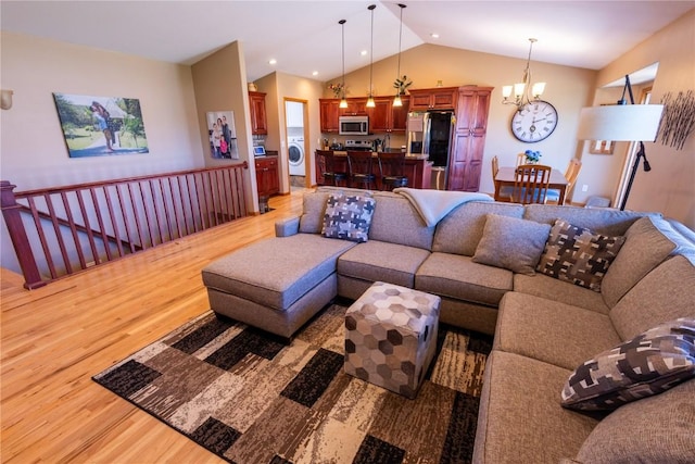 living room with washer / dryer, lofted ceiling, light wood-type flooring, and a notable chandelier