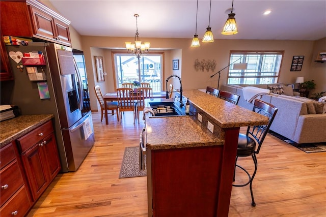 kitchen with a breakfast bar, stainless steel fridge, light wood finished floors, a chandelier, and open floor plan