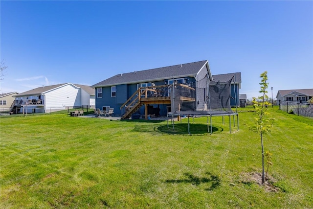 rear view of house featuring a lawn, a wooden deck, stairs, and a trampoline