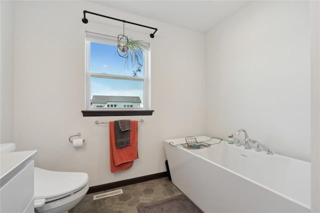bathroom with vanity, toilet, baseboards, visible vents, and a soaking tub