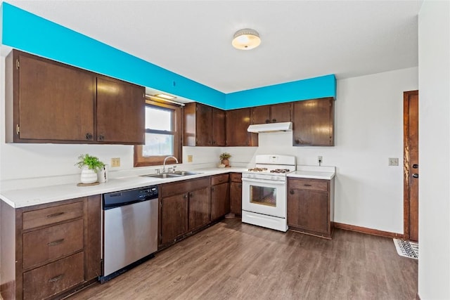kitchen with a sink, gas range gas stove, wood finished floors, stainless steel dishwasher, and under cabinet range hood