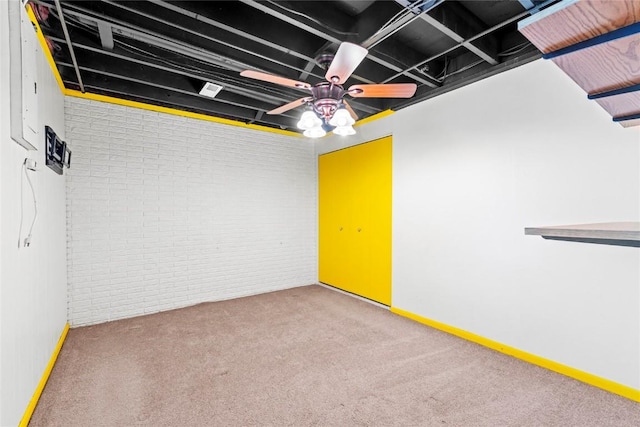 carpeted spare room with baseboards, a ceiling fan, and brick wall