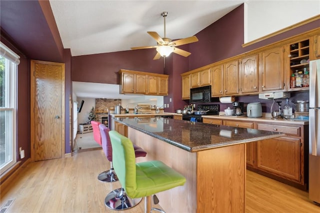 kitchen featuring ceiling fan, black appliances, light wood finished floors, and a kitchen breakfast bar